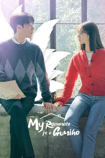 The poster features two characters in a cozy, sunlit room with a white, abstract sculpture in the background. The man wears a dark sweater with diamond patterns, while the woman dons a red cardigan over blue jeans. Their relaxed postures and warm lighting evoke a friendly, everyday atmosphere, hi...