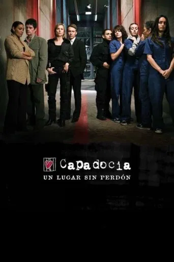The poster features a group of six characters standing in a dimly lit room, exuding mystery and intrigue. The muted tones of the image, with dark clothing and shadowy figures, create a suspenseful atmosphere. The title "Capadocia" is prominently displayed at the bottom, hinting at the show's dark...