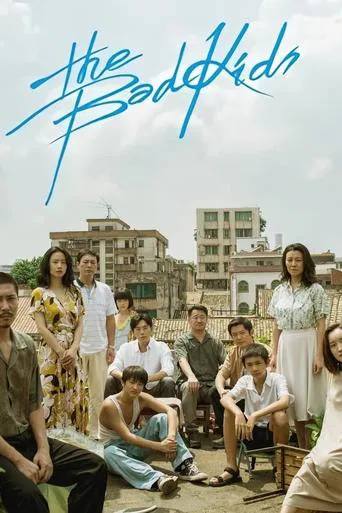The poster features a group of diverse young people in casual attire, sitting and standing in front of a backdrop of colorful buildings. The vibrant blue title text "The Bad Kids" stands out against the sky, suggesting a lively, possibly comedic tone. The overall mood is relaxed and youthful, cap...