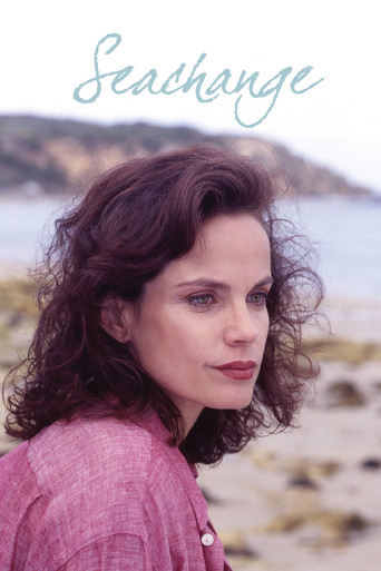 The poster features a woman with curly brown hair, wearing a pink shirt, gazing thoughtfully at the camera. The background shows a serene coastal scene with soft blues and warm tones. The title "SeaChange" is elegantly written in light blue script at the top, evoking a sense of calm and introspec...