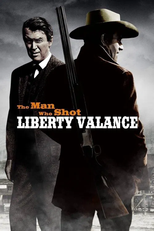 The poster features two men in a dramatic, moody atmosphere. One man in a dark suit stands on the left, while the other, wearing a cowboy hat and coat, holds a shotgun. The title "The Man Who Shot Liberty Valance" is prominently displayed in bold, white letters. The overall mood is intense and su...