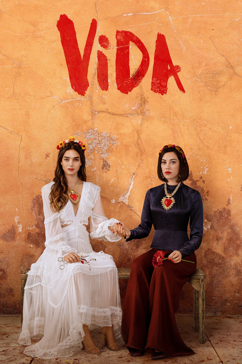 Two women in traditional attire sit against a warm, textured orange backdrop. The woman on the left wears a flowing white dress with a crown, while the woman on the right dons a dark blue top and maroon skirt. Their expressions convey a sense of quiet dignity and cultural pride. The bold red titl...