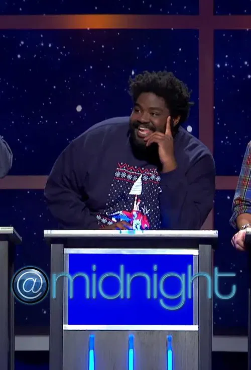 A comedian stands behind a podium at "Midnight with Chris Hardwick," laughing heartily while wearing a dark sweater with a colorful graphic. The starry backdrop suggests a night sky, and the cool blue tones of the set enhance the nighttime theme.