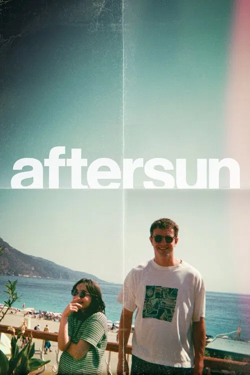The poster features a couple standing by the ocean, with the title "Aftersun" prominently displayed in bold white letters. The warm sunset hues blend into the cool blue sky, creating a serene and romantic atmosphere.