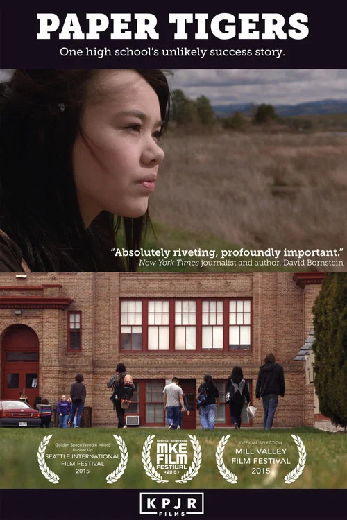 The poster features a young woman with a contemplative expression against a backdrop of a brick school building. The warm tones of the building contrast with the cool, muted colors of the surrounding landscape. A quote suggests the film explores the complexities of high school life. The overall m...