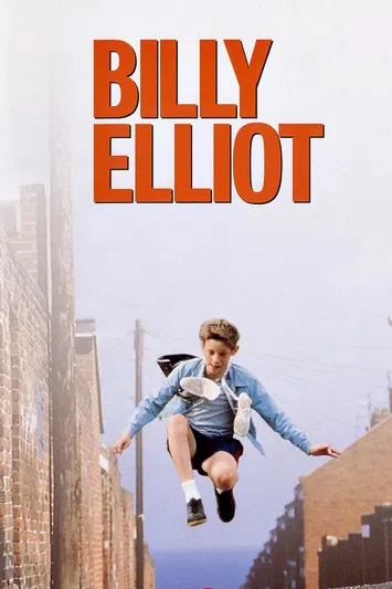 The poster features a young boy mid-air against a bright blue sky, wearing a vibrant blue jacket and black shorts. His shadow stretches below him on the green grass, symbolizing his journey and potential. The bold red text "Billy Elliot" anchors the image, evoking themes of ambition and self-disc...