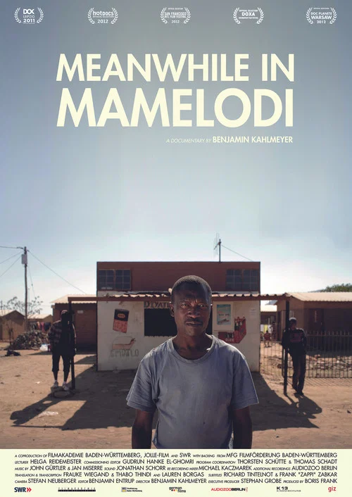 The poster features a man in a gray shirt standing in the foreground, with other figures in the background against a dusty, sunlit backdrop. The muted earth tones and warm lighting evoke a somber, reflective mood, suggesting themes of displacement and resilience.