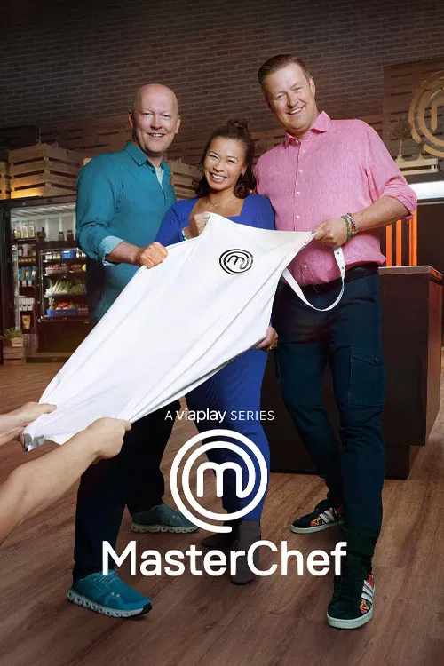 Three hosts pose proudly on a wooden floor, holding up a white MasterChef dish towel. Warm lighting and casual attire create a relaxed, friendly atmosphere. The image captures the essence of the show's fun and engaging spirit.
